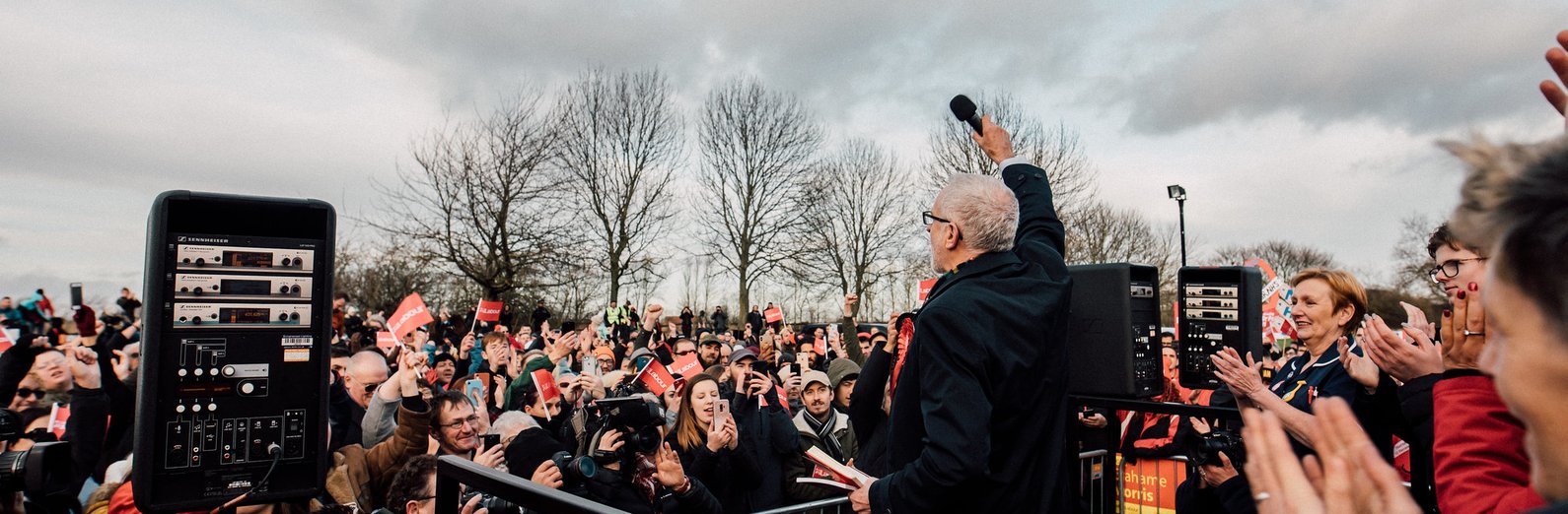 Jeremy Corby addressing crowd, lifting his microphone towards the people listening to him